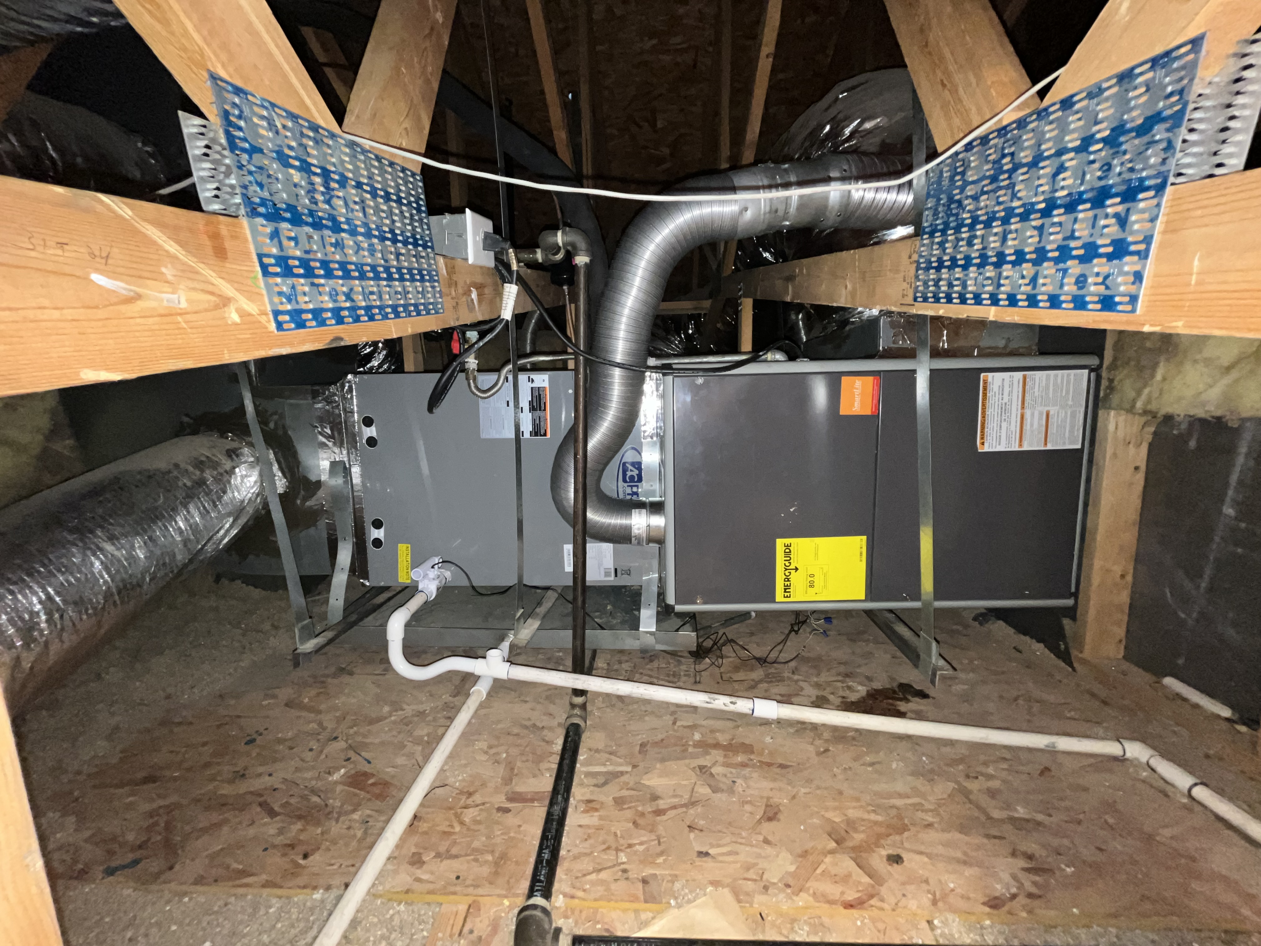 A professionally installed HVAC system in an attic space, featuring insulated ductwork, an air handler, and a condensate drainage system. The unit is securely m